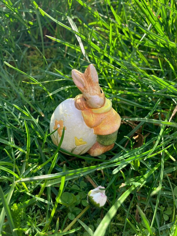 Osterhase lehnt sich an Osterei, die Figur steht auf einer Wiese.