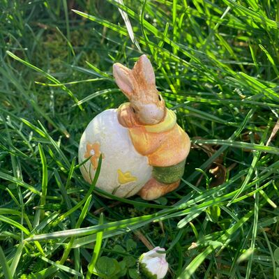 Osterhase lehnt sich an Osterei, die Figur steht auf einer Wiese.