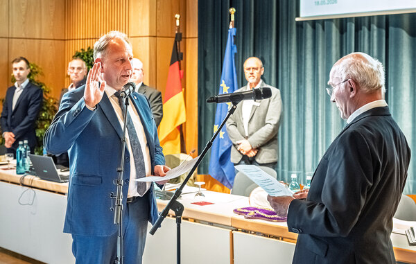 Markus Schlemmer legt seinen Amtseid ab. Er hat die rechte Hand gehoben zum Amtseid. Vor ihm steht Dr. Robert Löwer, das älteste anwesende Stadtratsmitglied und nimmt den Amtseid ab. 