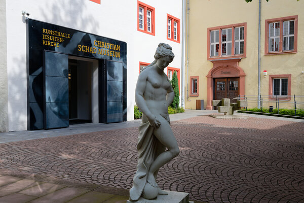 Innenhof mit Eingang Kunsthalle Jesuitenkirche und Schadmuseum. Im Vordergrund die Statue einer nackten Frau eine Toga haltend. 
