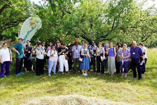 Gruppenfoto auf der Wiese unter Bäumen. Vertreterinnen und Vertreter südafrikanischer und deutscher Kommunen bei der Führung über eine Streuobstwiese mit dem Geschäftsführer der Schlaraffenburger GmbH Alexander Vorbeck (2.v.l.)  