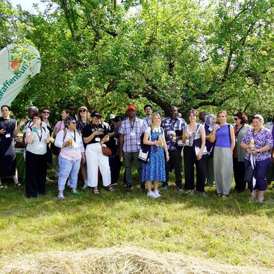 Bild vergr&ouml;&szlig;ern: Gruppenfoto auf der Wiese unter Bäumen. Vertreterinnen und Vertreter südafrikanischer und deutscher Kommunen bei der Führung über eine Streuobstwiese mit dem Geschäftsführer der Schlaraffenburger GmbH Alexander Vorbeck (2.v.l.)