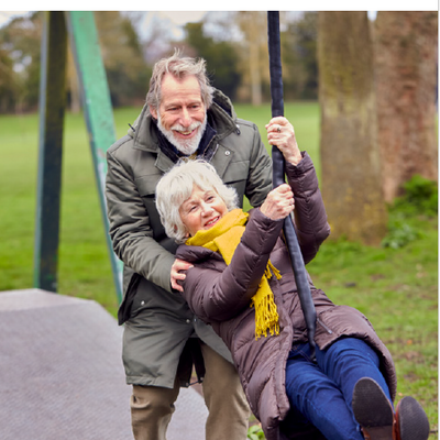 Ältere Menschen auf einem Spielplatz. Mann schubst Frau bei Kinderseilbahn an. 