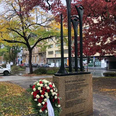 Bild vergr&ouml;&szlig;ern: Das Graslitzer Denkmal im Offenen Schöntal. Über einem Granit-Sockel erhebt sich eine Bronzegruppe aus drei nebeneinanderstehenden, stilisierten menschlichen Figuren
verschiedener Größen, die ihre Hände über dem Kopf verschränkt haben.